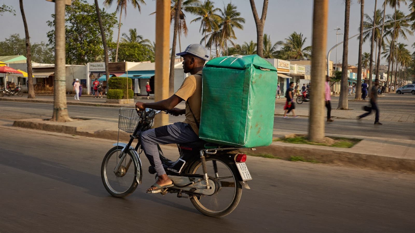 A delivery rider carrying a parcel box along a street in Accra at golden hour.