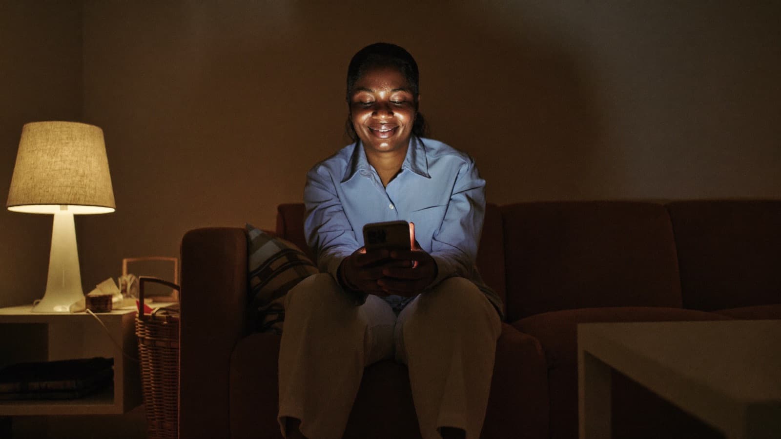A business owner sitting at home in the evening, reading her phone by lamplight.